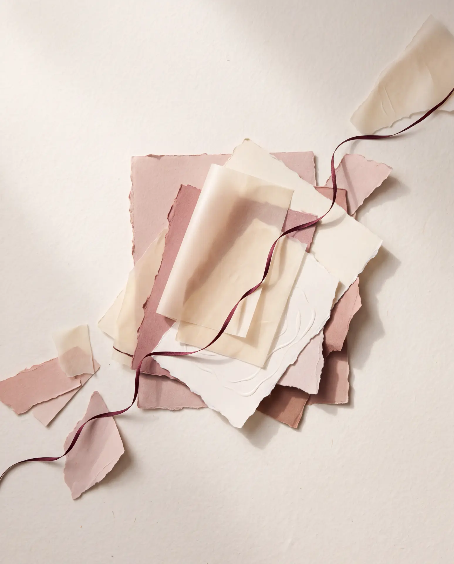 Torn papers in blush, ivory and rose tied with a burgundy ribbon