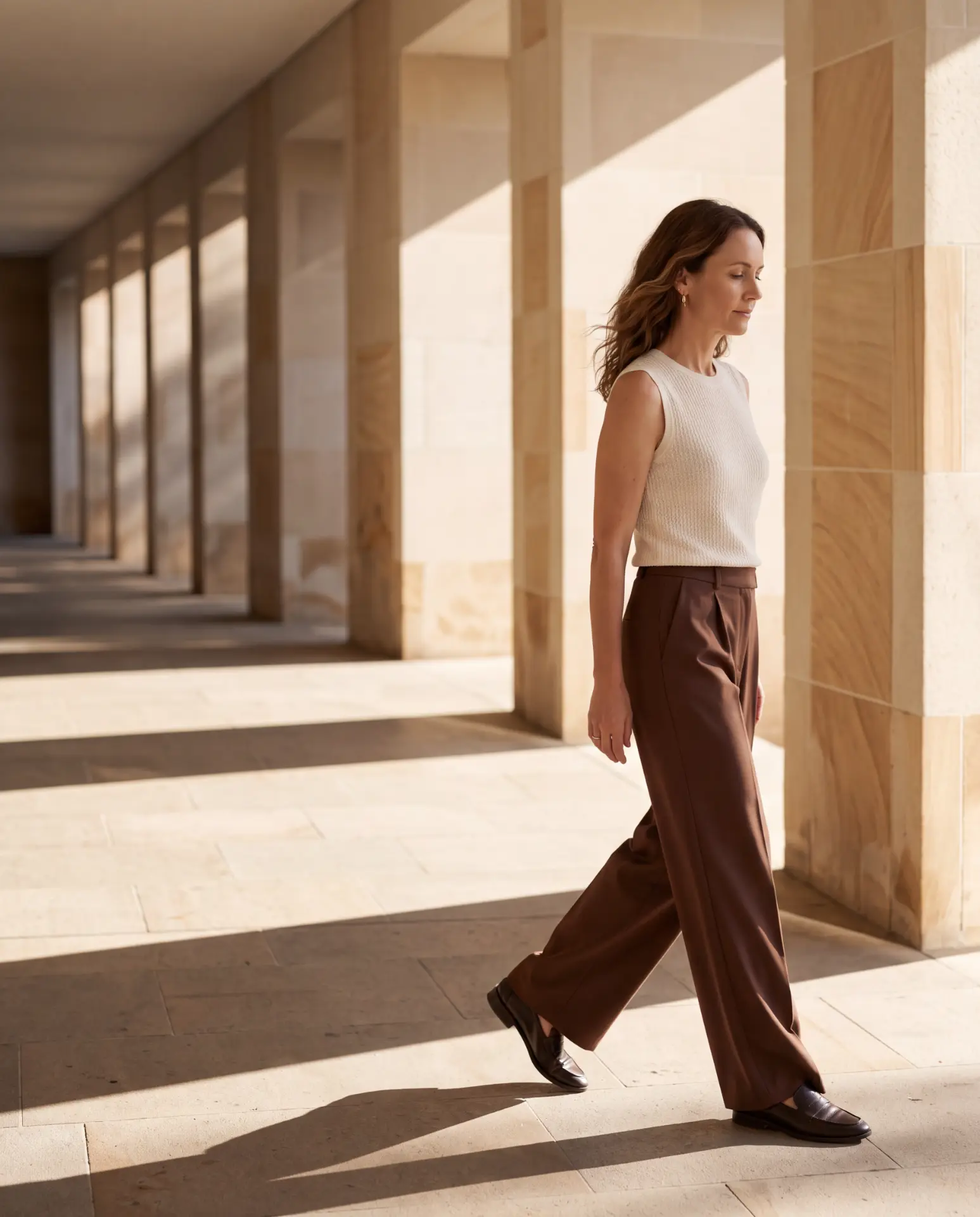 A woman walking with purpose through a sunlit sandstone colonnade